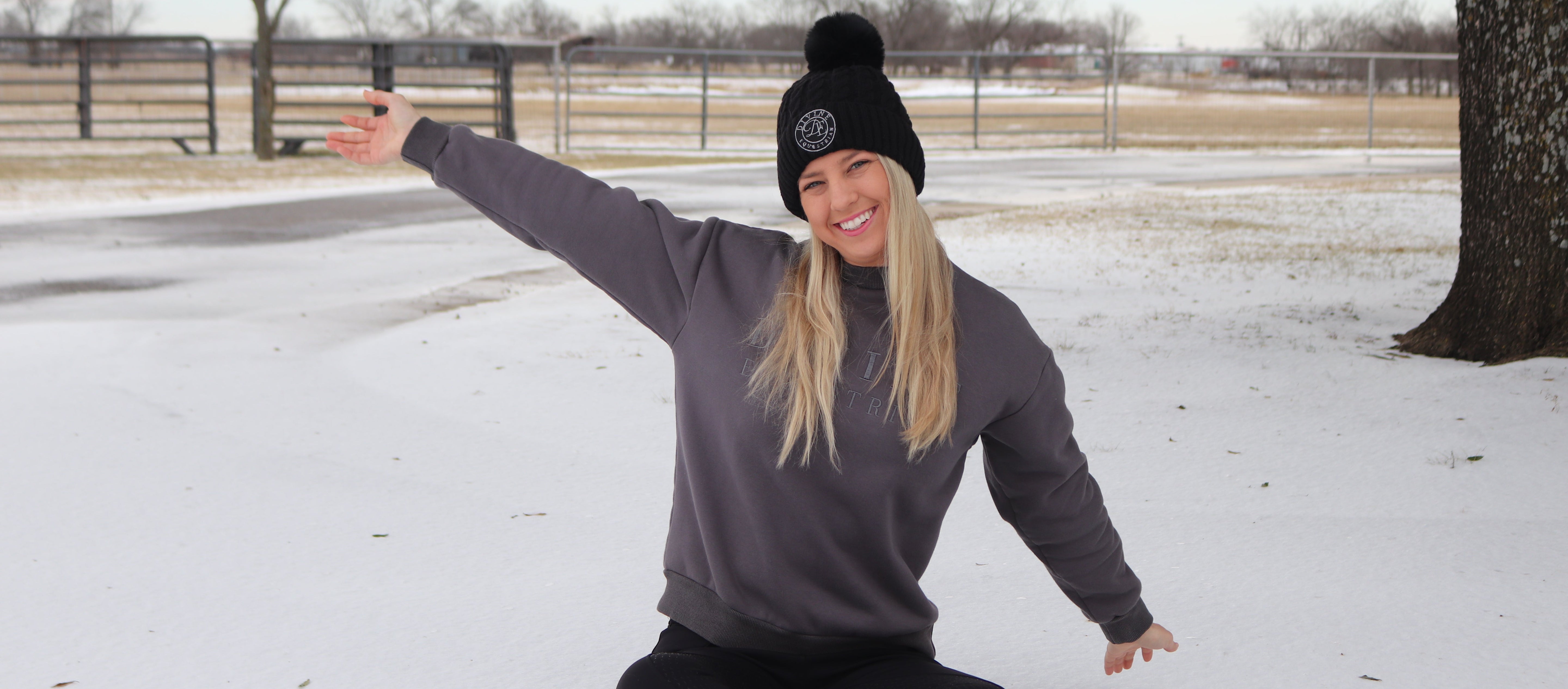 Person sitting on a log in a snowy landscape with a black beanie and gray sweatshirt.